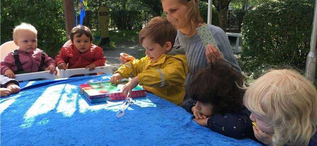 Voksen og børn ved bord på legepladsen i solskin