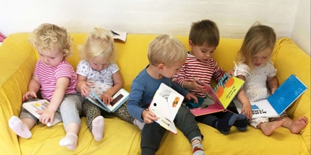 Fem børn sidder sammen i sofa og kigger i bøger