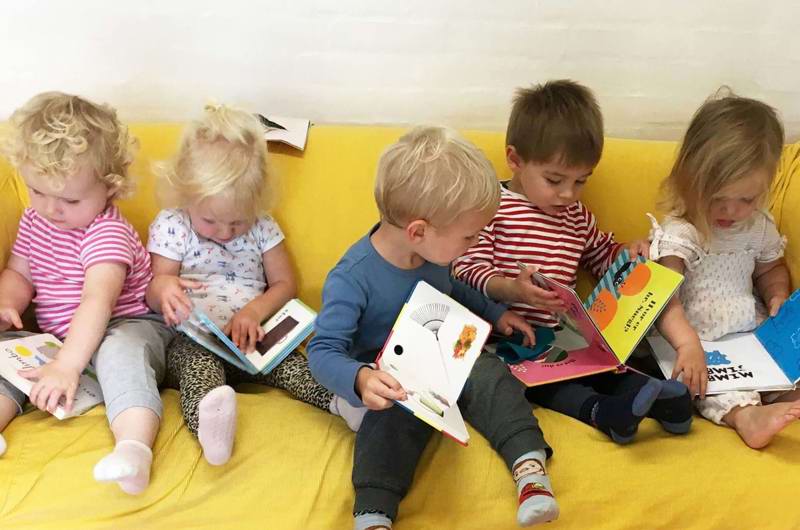 Fem børn sidder sammen i sofa og kigger i bøger