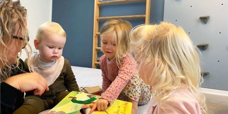 Voksen og tre børn læser bog på gulvet 
