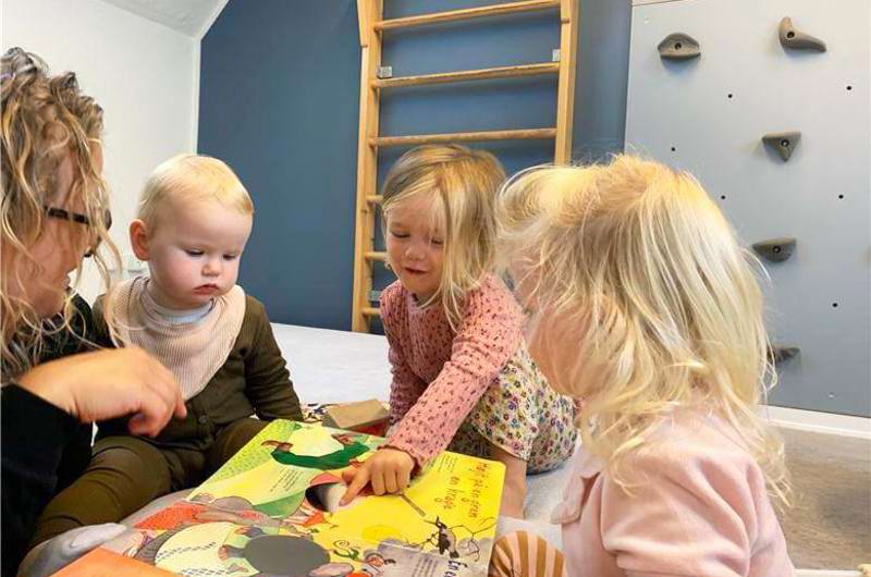 Voksen og tre børn læser bog på gulvet